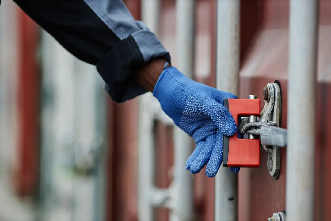 Close-up of a technician wearing protective blue gloves inspecting an automatic security gate latch and locking mechanism.