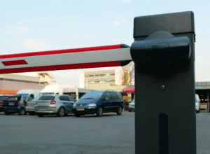 Close-up of a red and white barrier arm gate with parked cars in the background